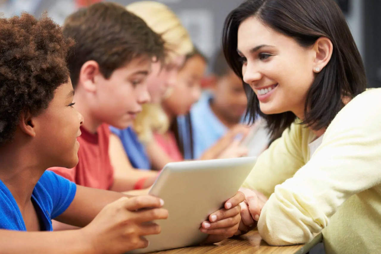 perfil-estudante-de-pedagogia - professora olhando para alunos que segura um tablet